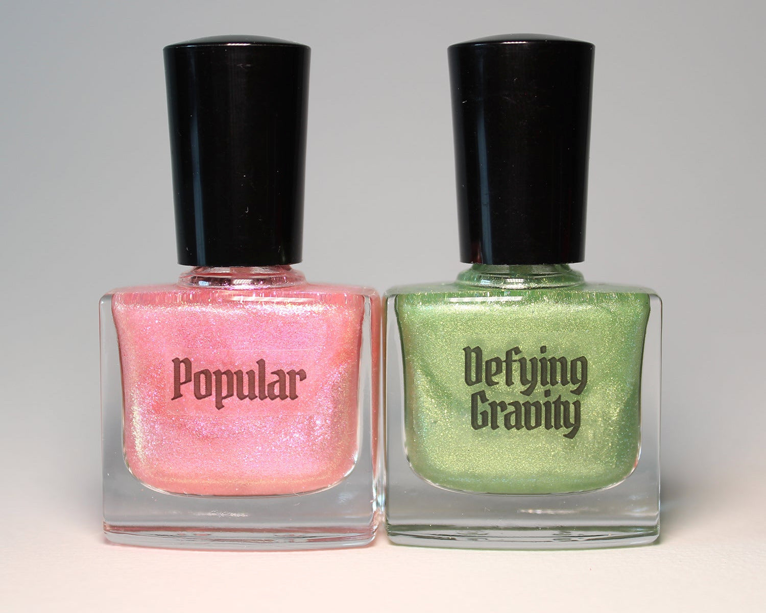 Two bottles of nail polish, one pink and one green, with black caps on a gray background.